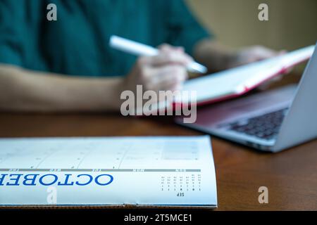 Calendar on top of wood table with blur woman looking at notepad at the background. Stock Photo