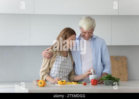 Senior family couple and pretty adult daughter preparing healthy dinner Stock Photo