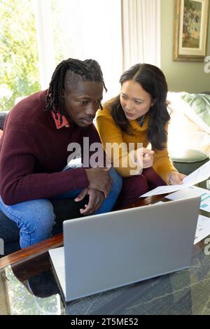 Serious diverse couple sitting on couch using laptop discussing bills and finances in living room Stock Photo