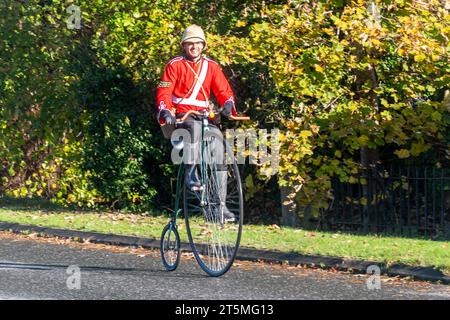 5th November 2023. Participants in the London to Brighton Veteran Car Run 2023 driving through West Sussex, England, UK. The route of the popular annual event runs for 60 miles. A man riding a penny farthing bicycle wearing a Victorian British Army tunic and helmet Stock Photo