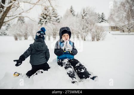 Two brothers play on snow pile while one boy sticks out tongue a Stock Photo