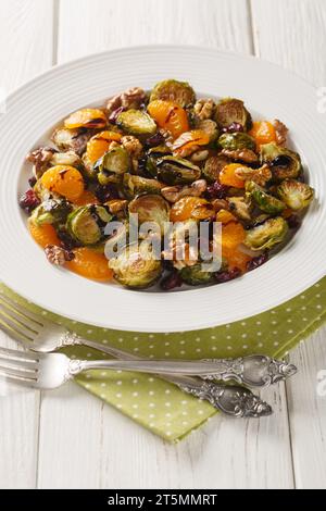 Baked Brussels sprouts with tangerines, walnuts and dried cranberries dressed with balsamic glaze close-up in a plate on the table. Vertical Stock Photo