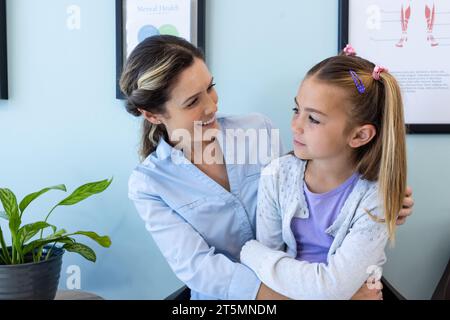 Happy caucasian daughter patient sitting on mother's lap talking in hospital waiting room Stock Photo