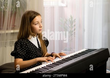 A concentrated young girl practices piano at home, immersed in music. Stock Photo
