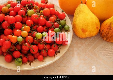 Cherry tomatoes and pears in a clay beige plate. Red farm tomatoes in rustic bowl. Stock Photo