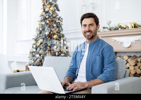 Portrait of a young businessman sitting at home and working on a laptop. He looks at the camera, smiles. Stock Photo