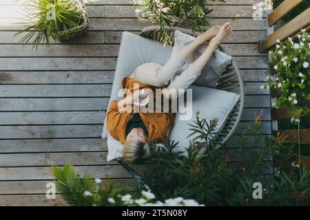 Top view of woman relaxing in the garden, drinking coffee and lying on patio chair. Mother having moment to herself while her child is sleeping. Stock Photo