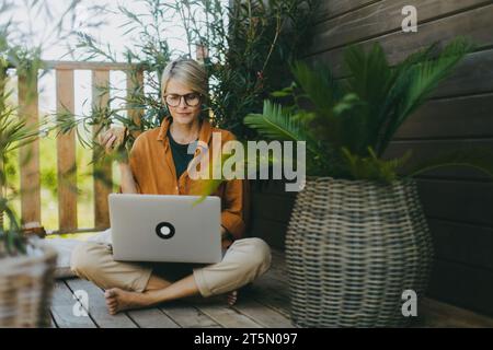 Woman working on laptop while eating sandwich. Businesswoman working remotely from outdoor homeoffice, having light lunch in the garden. Concept of Stock Photo