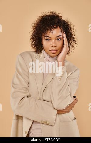 autumn fashion, stylish african american woman posing in turtleneck and blazer on beige backdrop Stock Photo