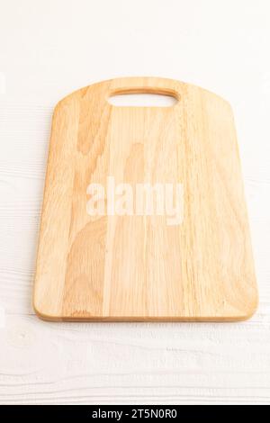 Empty rectangular wooden cutting board on white wooden background. Side view, close up. Stock Photo