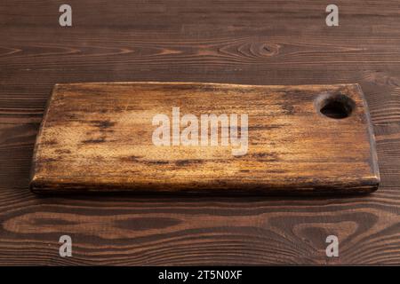 Empty rectangular wooden cutting board on brown wooden background. Side view, close up. Stock Photo