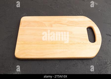 Empty rectangular wooden cutting board on black concrete background. Side view, close up Stock Photo