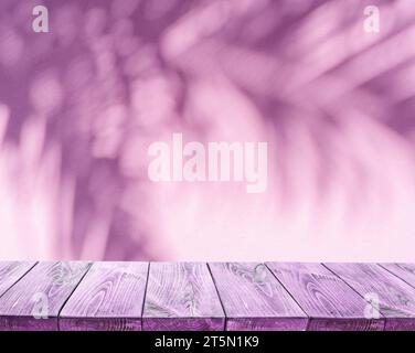 Blurred shadow of tropical palm leaves on pink wall and old planked table top in the foreground. Summer concept. Stock Photo