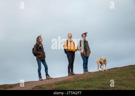 Three women and a dog in a very strong wind on top of the Skirrid, a distinctive hill near Abergavenny, Wales, UK, in the Brecon Beacons National Park Stock Photo