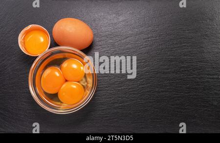 Brown chicken egg and egg yolks in glass bowl on natural stone black board. Flat lay. Stock Photo