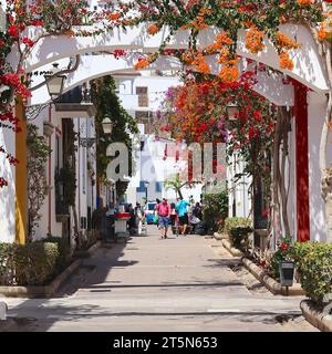 Vivid red,magenta & orange bougainvillea flowers cascade from arched sections above the intersection of several streets, Playa de Mogan, Gran Canaria. Stock Photo