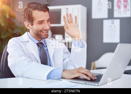 doctor waving hand to patient via laptop video link Stock Photo