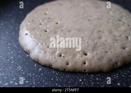 Closeup of a whole wheat with ground black sesame seeds pancake being fried in fry pan Stock Photo
