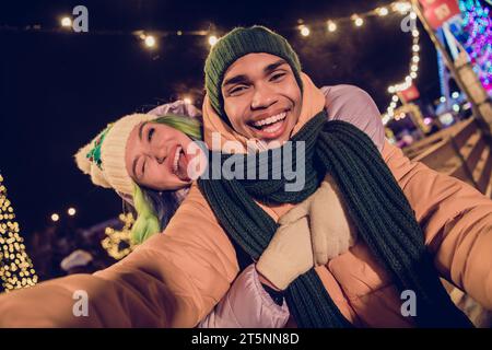 Photo of funny sweet african guy lady dressed coats winking recording x-mas video blog vlog together outdoors urban fair park Stock Photo