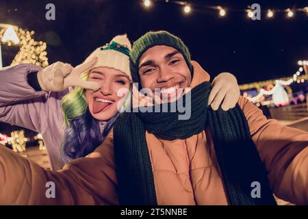 Photo of sweet cool african guy lady dressed coats showing v-sign winking recording x-mas video blog vlog together outdoors urban fair park Stock Photo