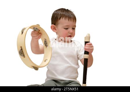 Toddler baby plays the flute sitting on the floor in the children's room, isolated on white background. Child boy playing musical instruments. Kid age Stock Photo