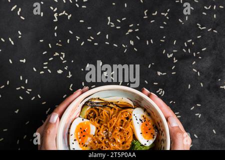 Close up woman s hand holding bowl noodles with boiled eggs rice grains black backdrop Stock Photo