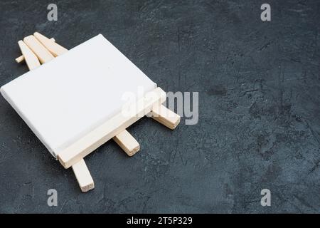 Small Easel with White Blank Cloth on a Wooden Table. Miniature