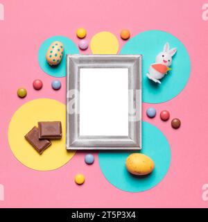 Empty frame surrounded with easter eggs bunny candies chocolate pieces pink backdrop Stock Photo