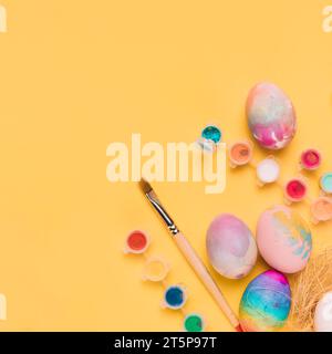 Overhead view painted easter eggs paint brush water color paint yellow backdrop Stock Photo