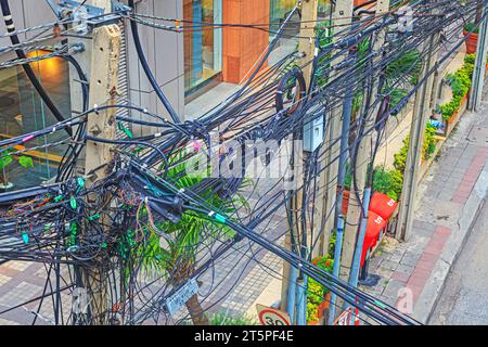 Chaotic cable routing of electricity and telephone cables on a main street in bangkok during daytime Stock Photo