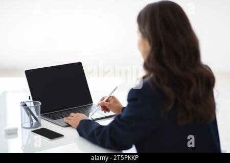 Woman using laptop and stylus while working in office Stock Photo