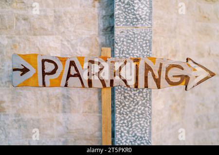 Wooden pointer with an arrow near the stone wall. Caption: Parking Stock Photo