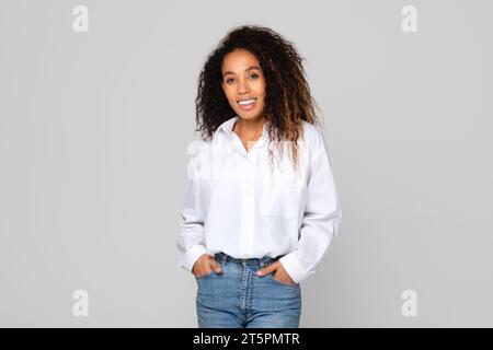 African American lady confidently smiling holding hands in pockets, studio Stock Photo