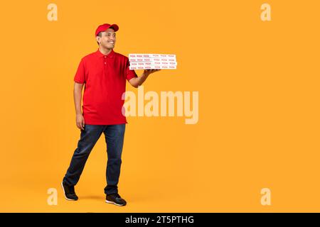 courier guy in uniform presents takeaway pizza boxes, yellow backdrop Stock Photo