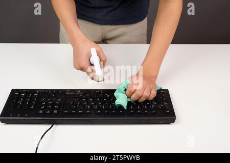 Cleaning computer keyboard in office, spraying water with a spray bottle dusty and dirty electronic, housework Stock Photo