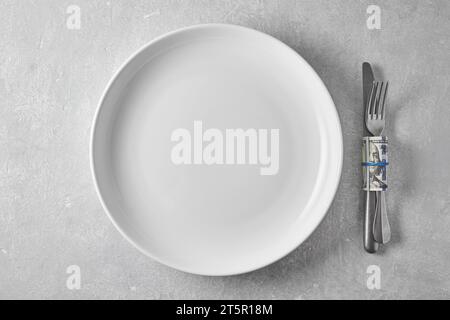 An empty white plate and a dinner fork and knife wrapped in a hundred dollar bill. Tips to the waiter in a restaurant. Stock Photo