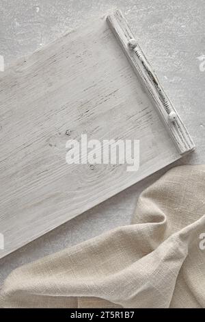 A fragment of a wooden white painted tray and a crumpled linen kitchen towel on a gray concrete table. Top view with copy space Stock Photo