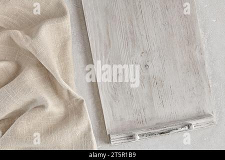 Fragment of a wooden white painted tray and a crumpled linen kitchen napkin on a light concrete table. Food menu mockup Stock Photo