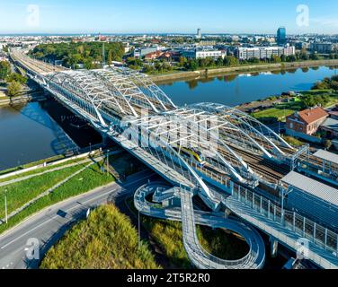 Fast city train on new triple tied arc railroad bridge with four tracks, footbridge and bike lane over Vistula river in Krakow, Poland, entering new K Stock Photo