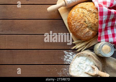 fresh bread with wheat ears and sack of flour, yeast, rolling pin on dark table, top view Stock Photo