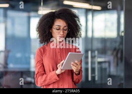 Serious concentrated and thinking woman using tablet computer, programmer standing near window, testing new software, using application. Stock Photo