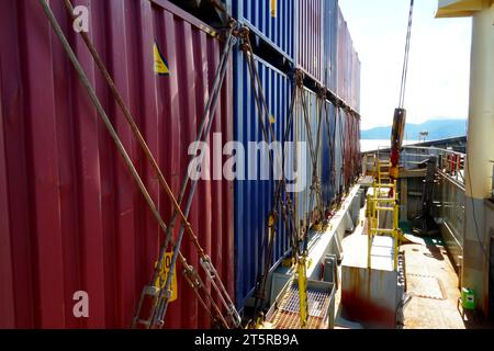 Row of lashed containers in a line with bars and twist locks situated in forward of container vessel with cranes. Stock Photo