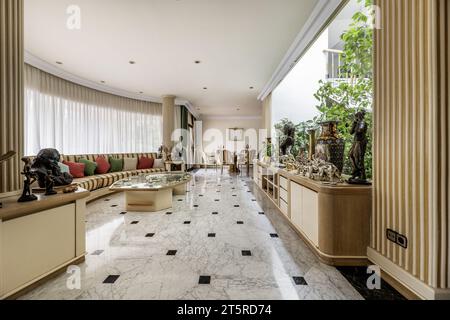 living rooms with perimeter sofa and staircase area of a luxury house with polished marble floors, golden metal railings and skylight with terrace Stock Photo