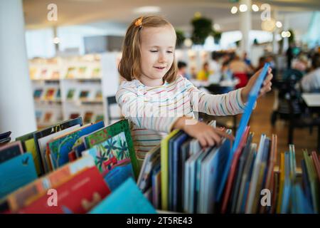 Five year old girl selecting a book in municipal library. Reading and learning concept Stock Photo
