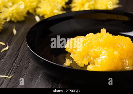 Crystallized honey in a black round plate on a dark wooden background, close-up. Stock Photo