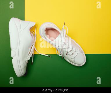 Top view of trendy white female sneakers with chunky platform soles on a green-yellow background. Fashionable stylish sports shoes Stock Photo