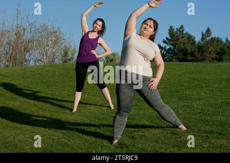Two middle-aged women doing fitness in city park, bending body to side. Healthy lifestyle, yoga, Pilates, weight loss. overweight woman doing yoga wit Stock Photo