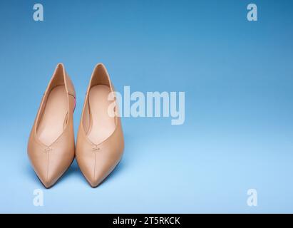 Elegant pointed-toe beige ballet flats at inclination on a gradient blue background. Fashion photography Stock Photo