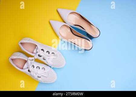 Two pairs of white women's summer shoes on a yellow-blue background. Top view, flat lay. Packing for summer travel concept Stock Photo