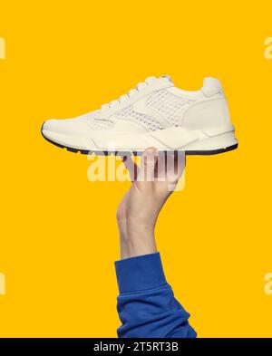 Hand holds white running sneaker on bright yellow background with copy space. Close up. Outlet marketing poster Stock Photo